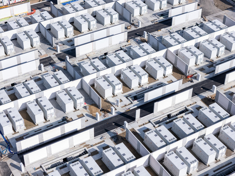Aerial view of a large scale battery energy storage system featuring rows of white containerized units separated by concrete walls and paved access paths in Poland.