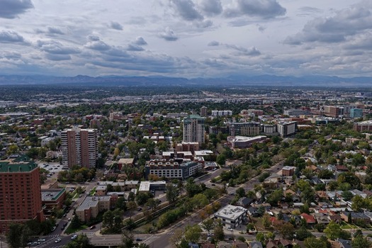 Aerial view of the Cherry Creek neighborhood featuring high rise buildings lush trees and urban infrastructure under a cloudy sky with distant mountains in Denver Colorado United States. Aerial view of the Cherry Creek neighborhood featuring high rise buildings lush trees and urban infrastructure under a cloudy sky with distant mountains in Denver Colorado United States.