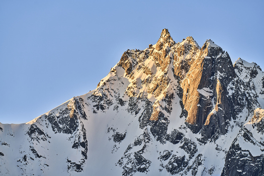 Aerial view of the snow covered Valchiavenna mountain peak illuminated by golden hour sunlight against a clear blue sky in Lombardia Italy. Aerial view of the snow covered Valchiavenna mountain peak illuminated by golden hour sunlight against a clear blue sky in Lombardia Italy.