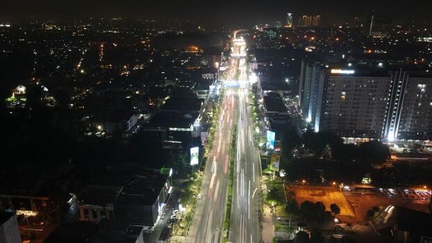 Aerial view of a busy urban highway at night with long exposure light trails from moving vehicles surrounded by illuminated buildings and city lights Bekasi Barat West Java Indonesia. Aerial view of a busy urban highway at night with long exposure light trails from moving vehicles surrounded by illuminated buildings and city lights Bekasi Barat West Java Indonesia.