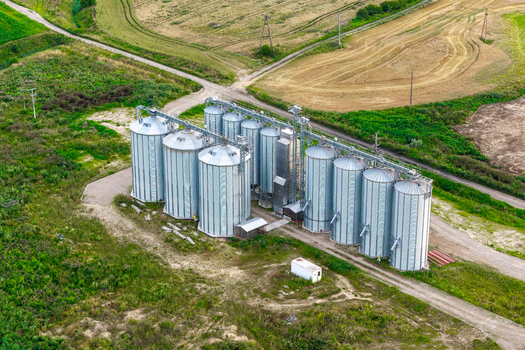 Aerial view of large metal grain bins situated in the middle of vast agricultural fields in Poland.