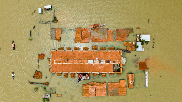 Aerial view of Baish Mowza Sarak Bazar partially submerged by floodwaters with small boats navigating the surrounding brown water in Nabinagar Chittagong Division Bangladesh. Aerial view of Baish Mowza Sarak Bazar partially submerged by floodwaters with small boats navigating the surrounding brown water in Nabinagar Chittagong Division Bangladesh.