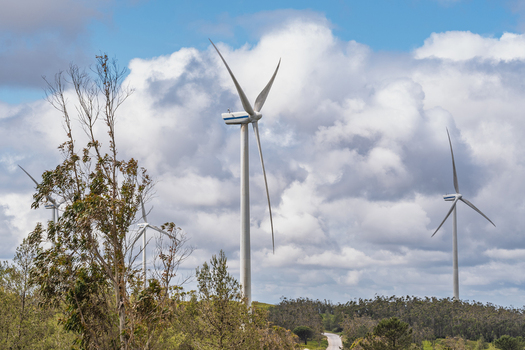 View of Parque Eolico da Serra dos Candeeiros with wind turbines rising above the trees under a cloudy blue sky in Rio Maior Santarem Portugal. View of Parque Eolico da Serra dos Candeeiros with wind turbines rising above the trees under a cloudy blue sky in Rio Maior Santarem Portugal.
