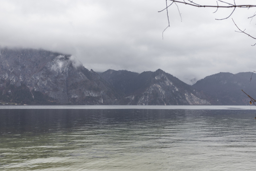 View of the calm Hallstatter See lake surrounded by misty alpine mountains under an overcast sky Hallstatt Upper Austria Austria. View of the calm Hallstatter See lake surrounded by misty alpine mountains under an overcast sky Hallstatt Upper Austria Austria.