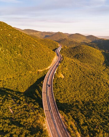 Aerial view of a winding highway cutting through lush green hills and dense forests under the warm light of the golden hour in Rijeka Primorje Gorski Kotar Croatia. Aerial view of a winding highway cutting through lush green hills and dense forests under the warm light of the golden hour in Rijeka Primorje Gorski Kotar Croatia.