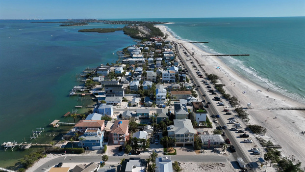 Aerial view of the coastal residential area featuring rows of houses a long sandy beach turquoise ocean waters and a coastal road with parked cars in Bradenton Florida United States.