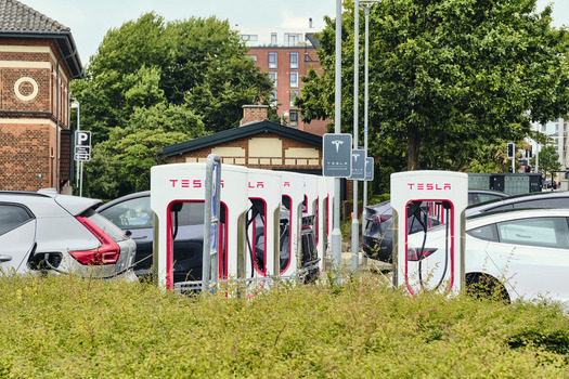 Esbjerg Denmark 25 July 2026 View of a Tesla Supercharger station with electric vehicles charging in a parking area surrounded by green bushes and trees in Esbjerg Denmark.