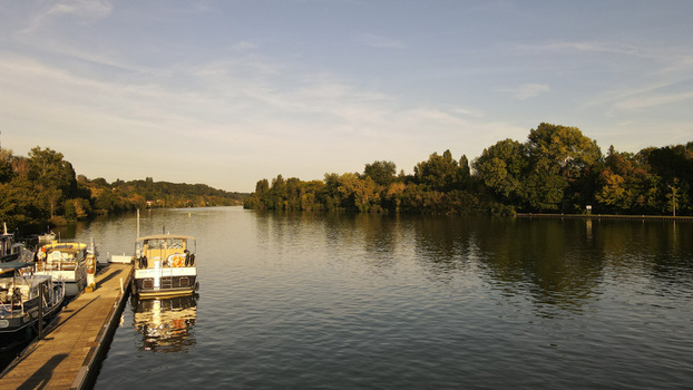Aerial view of boats moored at a wooden pier along the Seine river with dense trees lining the bank under a clear sky in Chartrettes Ile de France France. Aerial view of boats moored at a wooden pier along the Seine river with dense trees lining the bank under a clear sky in Chartrettes Ile de France France.