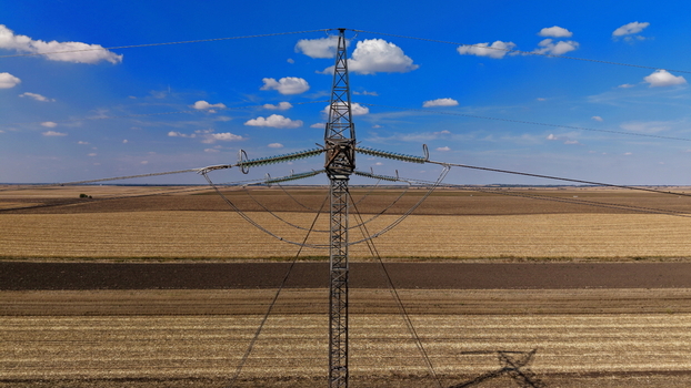 Aerial view of electric power transmission lines standing in a vast agricultural field under a clear blue sky in Pancevo Serbia.
