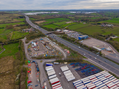 Aerial view of the M6 motorway passing through the Doxey Marshes with an industrial logistics yard filled with shipping containers and trucks in Stafford England United Kingdom. Aerial view of the M6 motorway passing through the Doxey Marshes with an industrial logistics yard filled with shipping containers and trucks in Stafford England United Kingdom.