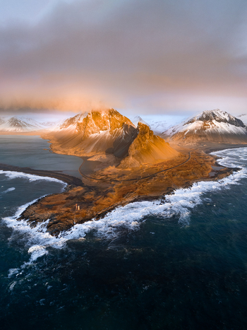 Aerial view of Hvalnes Lighthouse on the dramatic coastline near Eystrahorn mountain with snow capped peaks and crashing waves during golden hour in Sveitarfelagid Hornafjordur Iceland. Aerial view of Hvalnes Lighthouse on the dramatic coastline near Eystrahorn mountain with snow capped peaks and crashing waves during golden hour in Sveitarfelagid Hornafjordur Iceland.