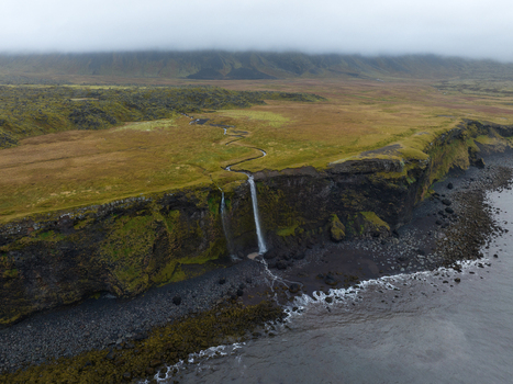 Aerial view of waterfalls cascade down rugged cliffs into the sea where the dark water meets the stark rocky beach Snæfellsnes Eyja og Miklaholtshreppur Iceland. Aerial view of waterfalls cascade down rugged cliffs into the sea where the dark water meets the stark rocky beach Snæfellsnes Eyja og Miklaholtshreppur Iceland.