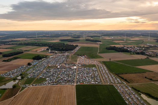 Aerial view of the Open Beatz Festival grounds with a large campsite and stages surrounded by green fields and wind turbines at sunset Herzogenaurach Bayern Germany. Aerial view of the Open Beatz Festival grounds with a large campsite and stages surrounded by green fields and wind turbines at sunset Herzogenaurach Bayern Germany.