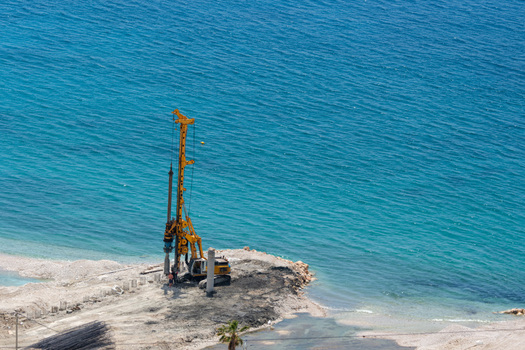 View of a yellow drilling rig operating on a coastal construction site by the turquoise sea in Vlore County Albania. View of a yellow drilling rig operating on a coastal construction site by the turquoise sea in Vlore County Albania.