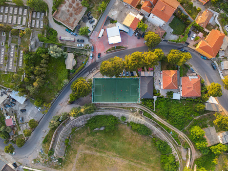 Aerial view of a green football pitch and an ancient stone amphitheater surrounded by orange rooftops and lush trees during golden hour in Kruje Durres County Albania.