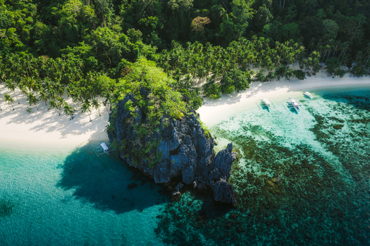 Aerial view of Papaya Beach featuring a prominent limestone rock formation surrounded by turquoise waters coral reefs and lush palm trees in El Nido Mimaropa Philippines. Aerial view of Papaya Beach featuring a prominent limestone rock formation surrounded by turquoise waters coral reefs and lush palm trees in El Nido Mimaropa Philippines.