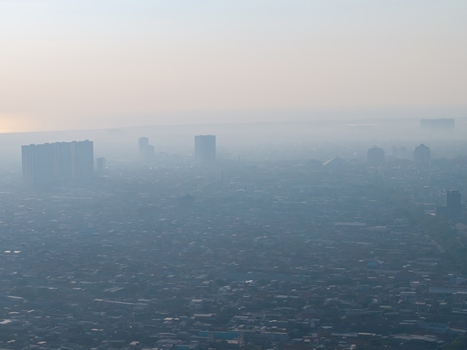 Aerial view of the sprawling cityscape shrouded in thick morning haze with tall residential towers rising above the dense urban fabric in Surabaya East Java Indonesia. Aerial view of the sprawling cityscape shrouded in thick morning haze with tall residential towers rising above the dense urban fabric in Surabaya East Java Indonesia.