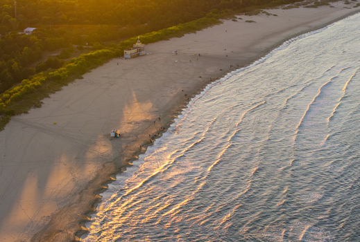 Aerial view of the sandy beach along the Baltic Sea with people walking near the shoreline and a building nestled in the dunes during golden hour in Gdansk Pomeranian Voivodeship Poland.