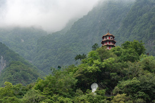 View of the Changchun Shrine pagoda nestled among lush green mountains and mist in Taroko National Park with a white statue visible below Xiulin Township Hualien County Taiwan.