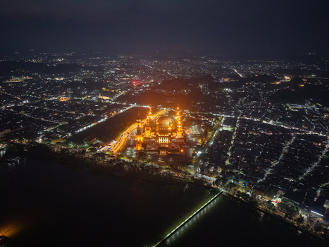Aerial view of Baitul Muttaqien Mosque illuminated at night surrounded by the glowing city lights of Samarinda and the Mahakam River in Samarinda East Kalimantan Indonesia.