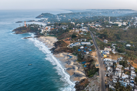 Aerial view of the iconic Vizhinjam Lighthouse standing on the rocky coastline with sandy beaches crashing waves and surrounding coastal buildings in Kovalam Keralam India. Aerial view of the iconic Vizhinjam Lighthouse standing on the rocky coastline with sandy beaches crashing waves and surrounding coastal buildings in Kovalam Keralam India.