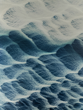 Aerial view of undulating snow covered terrain the stark white contrasting with deep blue shadows creating a mesmerizing otherworldly landscape Iceland Iceland. Aerial view of undulating snow covered terrain the stark white contrasting with deep blue shadows creating a mesmerizing otherworldly landscape Iceland Iceland.
