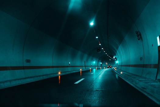 View of a car driving through a modern illuminated road tunnel with teal lighting in Greece.