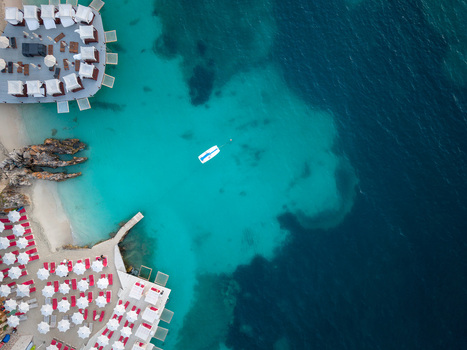Aerial view of a beach resort with white cabanas red umbrellas and a small boat floating in transparent turquoise water Ksamil Vlore County Albania. Aerial view of a beach resort with white cabanas red umbrellas and a small boat floating in transparent turquoise water Ksamil Vlore County Albania.