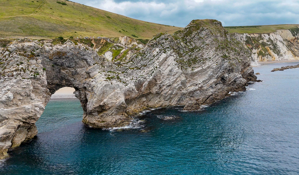 Aerial view of the limestone arch of Durdle Door on the Jurassic Coast featuring rugged cliffs turquoise sea and grassy hills in Wareham England United Kingdom. Aerial view of the limestone arch of Durdle Door on the Jurassic Coast featuring rugged cliffs turquoise sea and grassy hills in Wareham England United Kingdom.