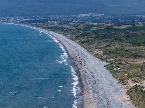 Aerial view of the pebble beach in Newcastle with people walking along the shore gentle waves and green hills in the background Newcastle Northern Ireland United Kingdom. Aerial view of the pebble beach in Newcastle with people walking along the shore gentle waves and green hills in the background Newcastle Northern Ireland United Kingdom.