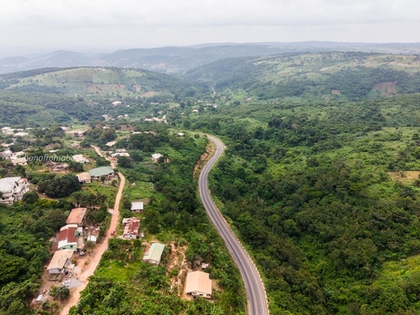Aerial view of a winding road cutting through a lush green hilly landscape with scattered houses in Ghana. Aerial view of a winding road cutting through a lush green hilly landscape with scattered houses in Ghana.