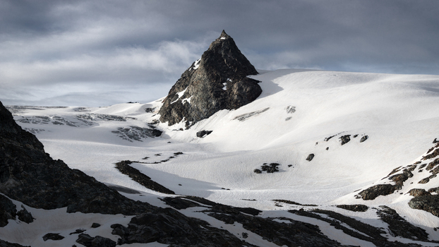 View of a sharp rocky mountain peak rising above a vast glacier and snow covered slopes under a cloudy sky in Aosta Valley Italy. View of a sharp rocky mountain peak rising above a vast glacier and snow covered slopes under a cloudy sky in Aosta Valley Italy.