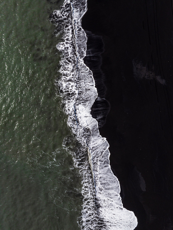 Aerial view of the dramatic contrast between the dark volcanic black sand beach and the white crashing waves of the Atlantic Ocean in Iceland. Aerial view of the dramatic contrast between the dark volcanic black sand beach and the white crashing waves of the Atlantic Ocean in Iceland.