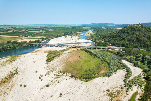 Aerial view of the Ponte Crescentino bridge spanning a river affected by severe drought with exposed dry riverbed sparse water flow and green hills in Verrua Savoia Piemonte Italy. Aerial view of the Ponte Crescentino bridge spanning a river affected by severe drought with exposed dry riverbed sparse water flow and green hills in Verrua Savoia Piemonte Italy.