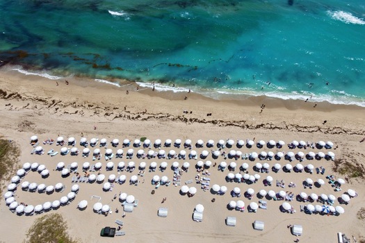 Aerial view of Singer Island beach featuring rows of white umbrellas along the sandy shore and turquoise ocean water in Riviera Beach Florida United States. Aerial view of Singer Island beach featuring rows of white umbrellas along the sandy shore and turquoise ocean water in Riviera Beach Florida United States.