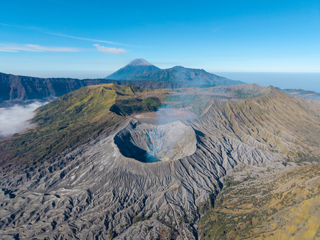 Aerial view of Mount Bromo crater with rugged volcanic slopes surrounding caldera and distant peaks under a clear blue sky in Tosari East Java Indonesia.