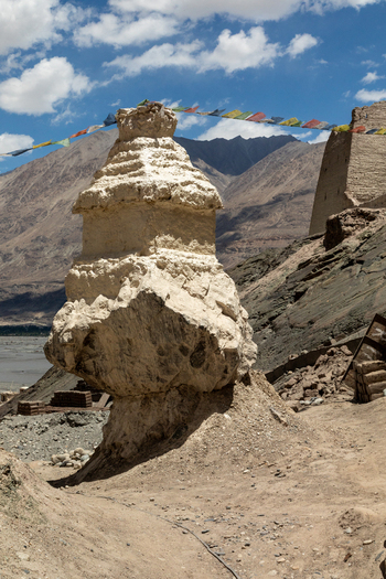 View of the ancient stupa at Charasa Gonpa adorned with colorful prayer flags against a backdrop of rugged mountains and a clear blue sky in Charasa Ladakh India.