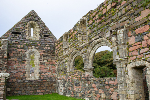 View of the ancient stone ruins of Iona Nunnery with arched windows and weathered masonry under a cloudy sky in Baile Mor Scotland United Kingdom. View of the ancient stone ruins of Iona Nunnery with arched windows and weathered masonry under a cloudy sky in Baile Mor Scotland United Kingdom.