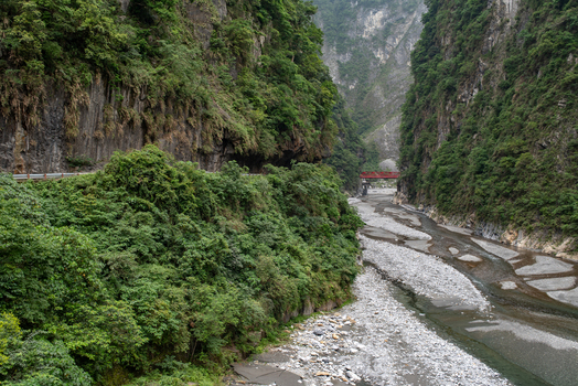 View of Taroko National Park featuring a deep river gorge with steep lush green cliffs a rocky riverbed and a red bridge in Xiulin Township Hualien County Taiwan.