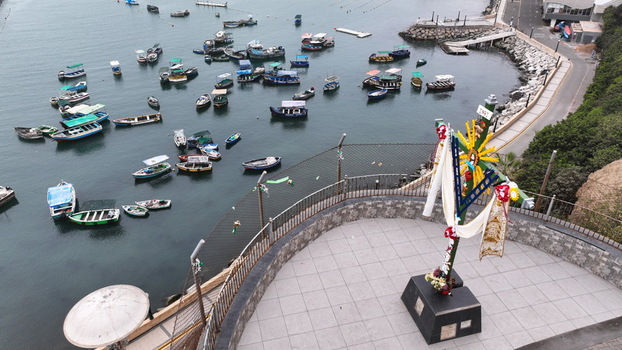 Aerial view of the bay of Chorrillos with many small fishing boats anchored in calm waters and a paved viewpoint area featuring a religious cross monument. Chorrillos Lima Province Peru.