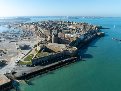 Aerial view of the ancient walled city its ramparts kissed by the turquoise sea with the spire of Saint Malo Cathedral piercing the clear blue sky Saint Malo Brittany France. Aerial view of the ancient walled city its ramparts kissed by the turquoise sea with the spire of Saint Malo Cathedral piercing the clear blue sky Saint Malo Brittany France.