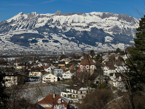 View of Vaduz town with traditional houses and snow covered mountains in the background under a clear blue sky in Vaduz Vaduz Liechtenstein.