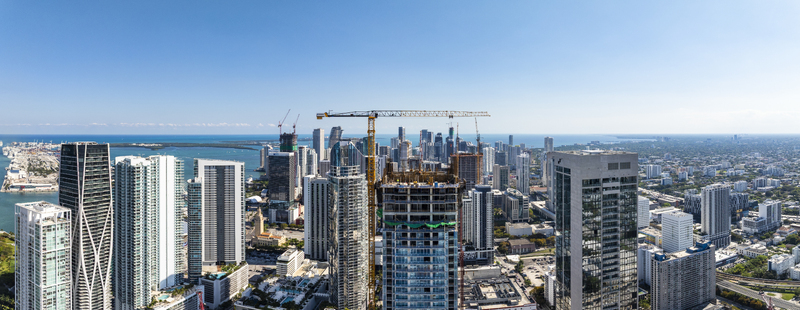 Aerial view of gleaming skyscrapers piercing the clear blue sky above Biscayne Bay with construction cranes dotting the skyline Miami Florida USA. Aerial view of gleaming skyscrapers piercing the clear blue sky above Biscayne Bay with construction cranes dotting the skyline Miami Florida USA.