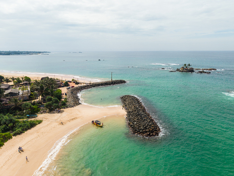 Aerial view of turquoise ocean waves hitting a sandy beach with stone breakwaters and a small boat in Peraliya Southern Province Sri Lanka. Aerial view of turquoise ocean waves hitting a sandy beach with stone breakwaters and a small boat in Peraliya Southern Province Sri Lanka.