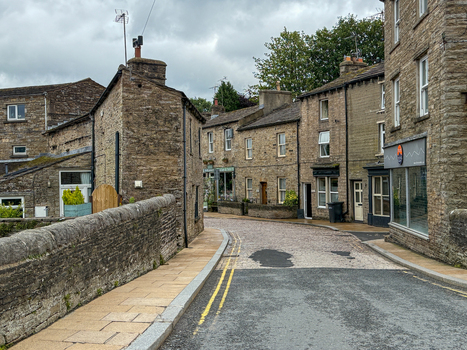 View of traditional stone buildings and a narrow street under a cloudy sky in Hawes England United Kingdom. View of traditional stone buildings and a narrow street under a cloudy sky in Hawes England United Kingdom.
