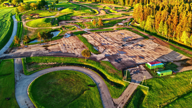Aerial view of a go kart racing track surrounded by lush green fields and dense forest during the golden hour in Latvia. Aerial view of a go kart racing track surrounded by lush green fields and dense forest during the golden hour in Latvia.
