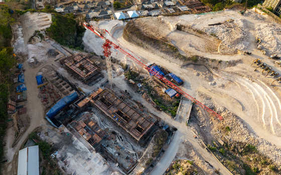 Aerial view of a resort development construction site with a large red tower crane concrete foundations and excavated earth in Kecamatan Kuta Selatan Bali Indonesia. Aerial view of a resort development construction site with a large red tower crane concrete foundations and excavated earth in Kecamatan Kuta Selatan Bali Indonesia.
