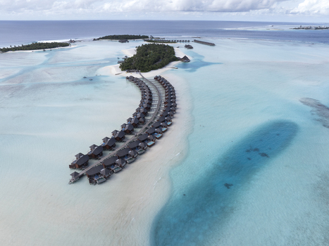 Aerial view of an overwater bungalow resort surrounded by turquoise lagoon waters and white sand beaches in the Maldives. Aerial view of an overwater bungalow resort surrounded by turquoise lagoon waters and white sand beaches in the Maldives.