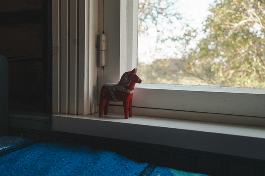 Laane County Estonia 19 May 2025 View of a red Dala horse figurine on a wooden windowsill in Vormsi with soft light and blurred trees visible through the window.