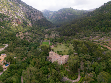 Aerial view of a historic stone manor nestled in a lush green valley surrounded by forested mountains and terraced fields Valldemossa Balearic Islands Spain.